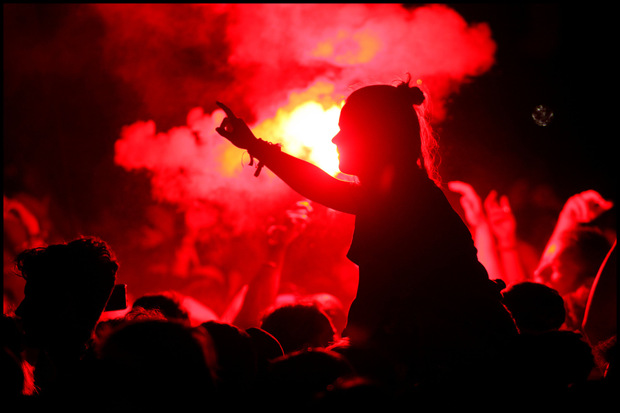 A young woman is illuminated by a flare in the crowd at The Glastonbury Festival.
