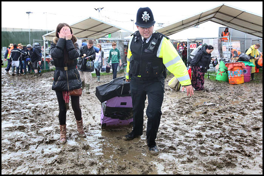 A policeman helps a reveller through the mud with her luggage as she arrives at the Glastonbury Festival.